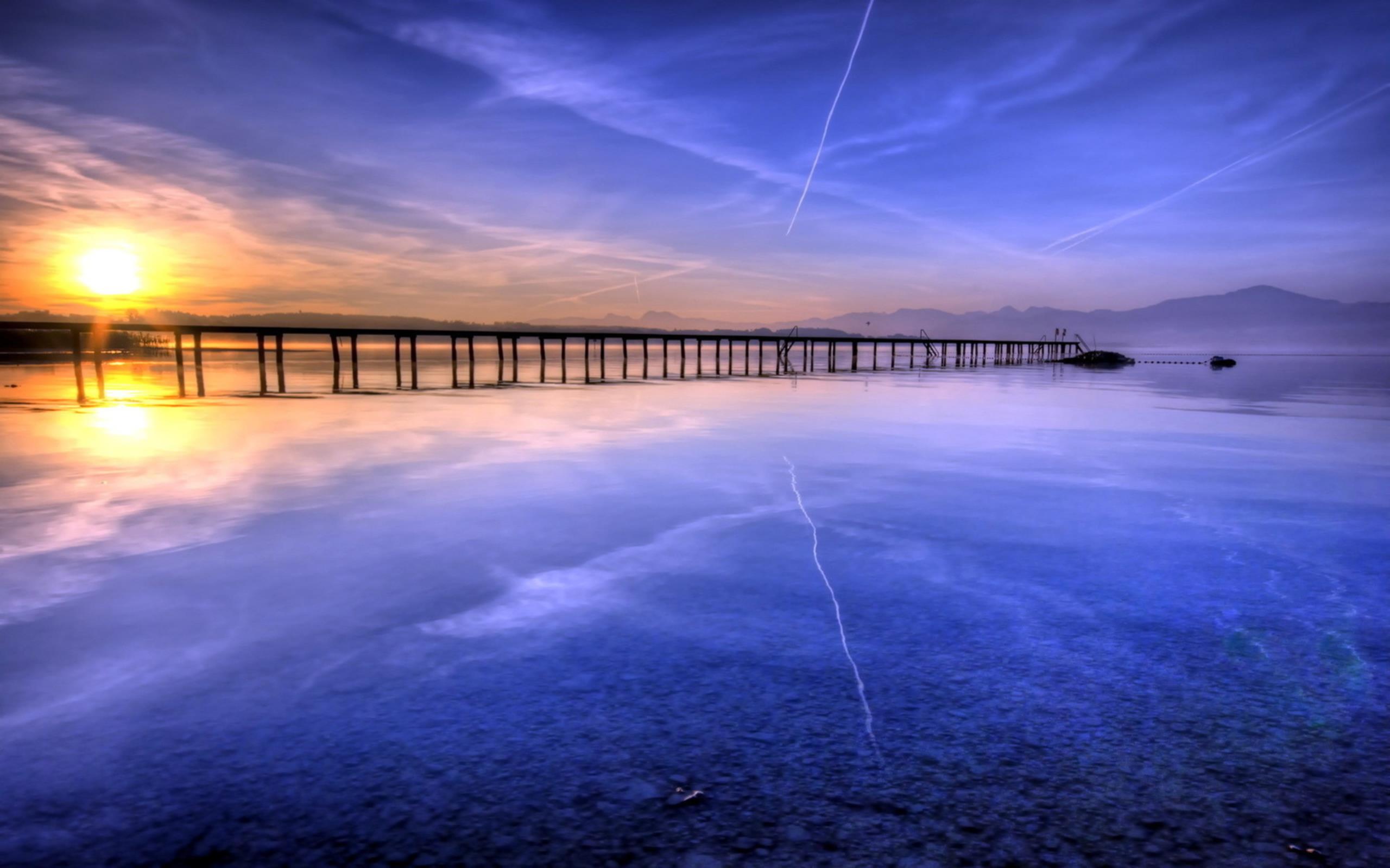 A bridge over an icy lake with sunset in the top left corner.